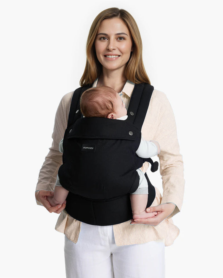 Translation missing: fr.Momcozy PureHug Baby Carrier. Black carrier, comfortable design, worn by mother holding baby. Ideal for babywearing